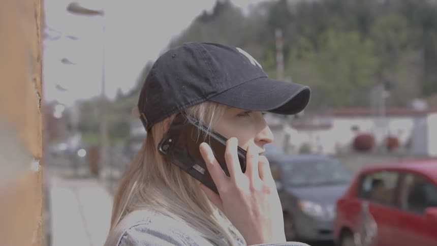 A woman in a ball cap talking on a black smartphone while standing outdoors