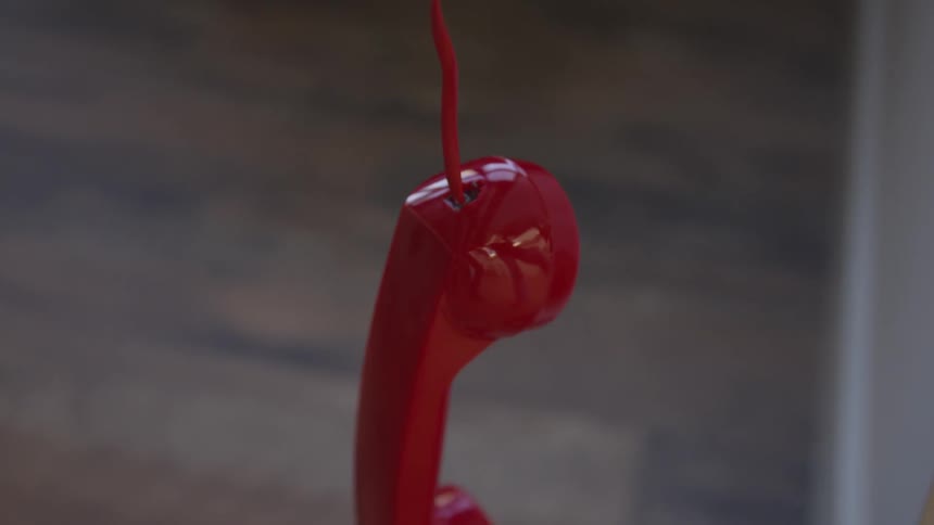 Red phone handset hands by cord over wooden floor