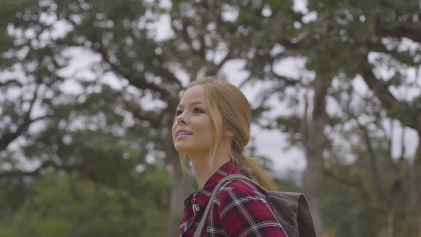 Woman looks around at trees while standing in a field