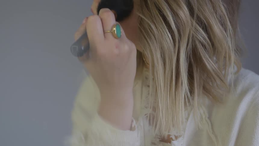 Blonde woman applying makeup to her face using a pencil