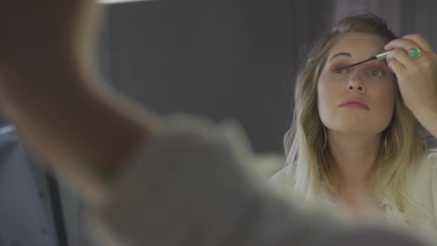 A woman looks in the mirror as she applies mascara