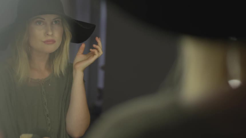 A woman looks in the mirror and plays with her hair and touches her sun hat