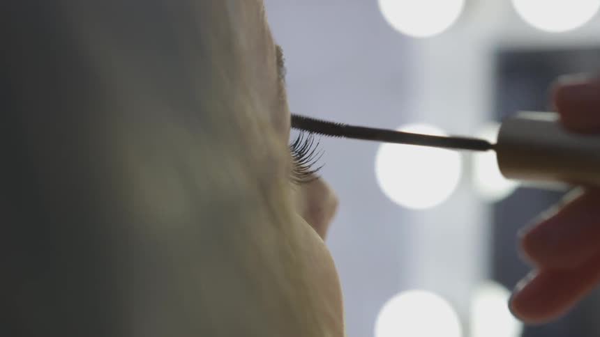 White woman applying eyeliner on eyelid with pencil