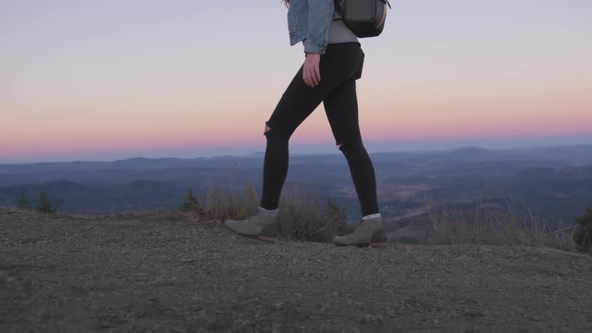 Woman hikes along hilltop overlooking valley at sunset