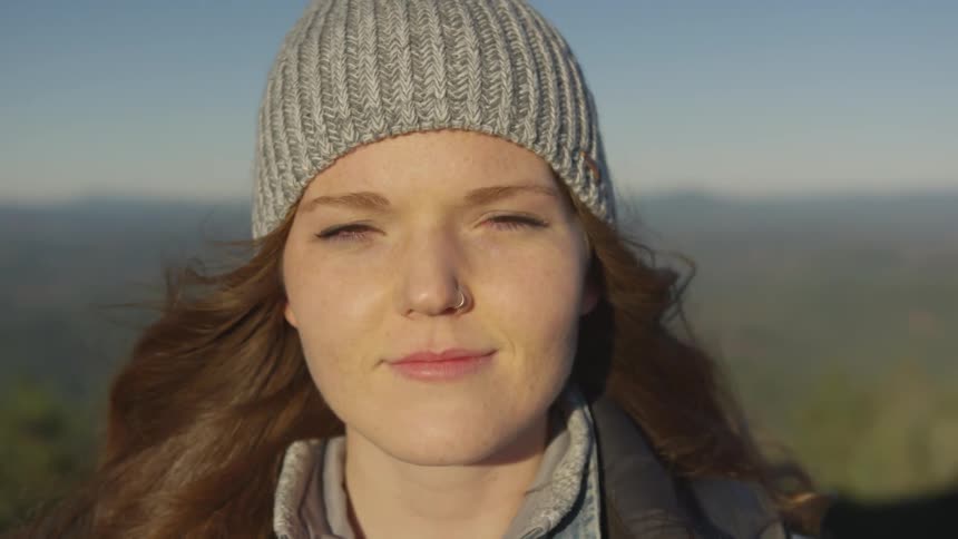 Woman wearing knit hat stands with sun on her face