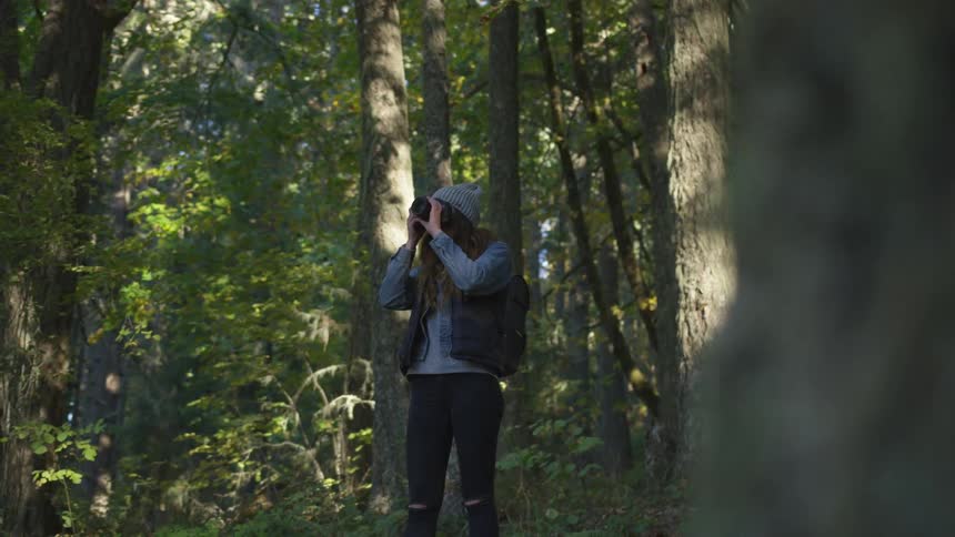 Woman wearing wooly hat takes pictures in nature with professional camera