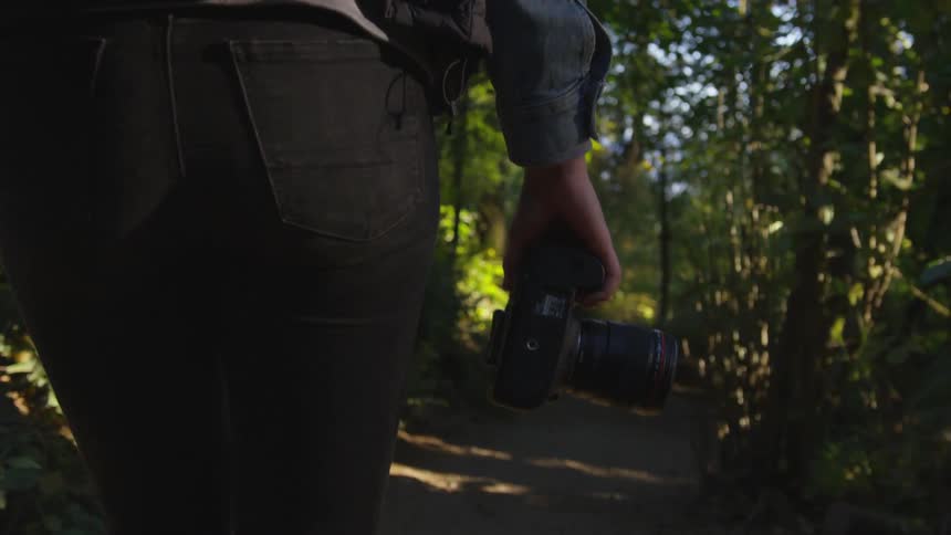 Woman walking on a dirt path through the forest with a camera in hand