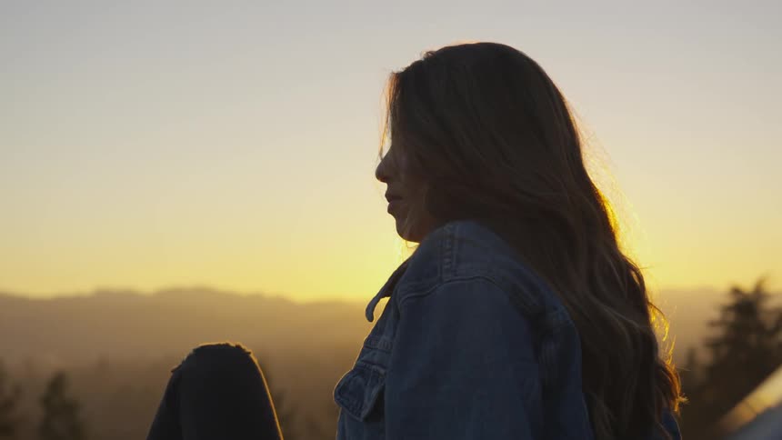 A blonde white woman sits in the wilderness and gazes out over the scenery