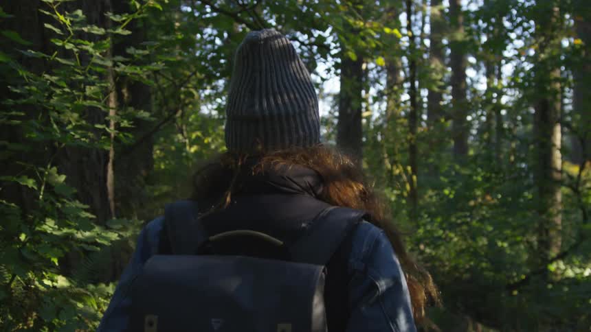 A woman wearing a backpack walking through a forest