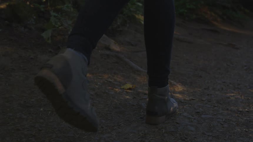 A hiker in boots walks on a dirt path in a forest