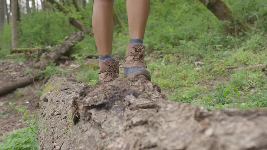 A woman wearing hiking boots walks on a fallen log