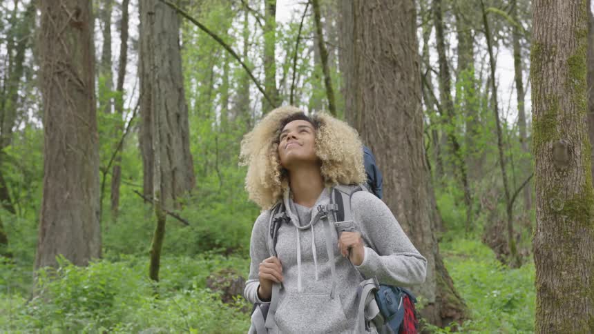 Woman stands in forest looking at sky