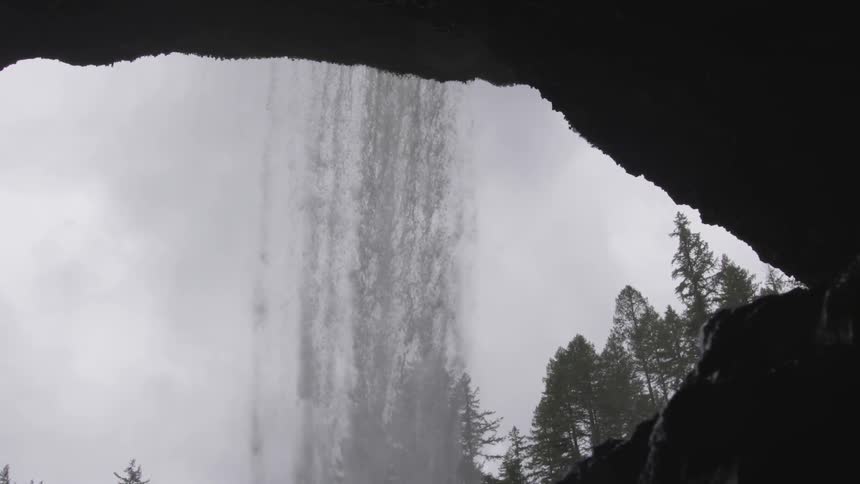 A waterfall cascades down over the mouth of a cave