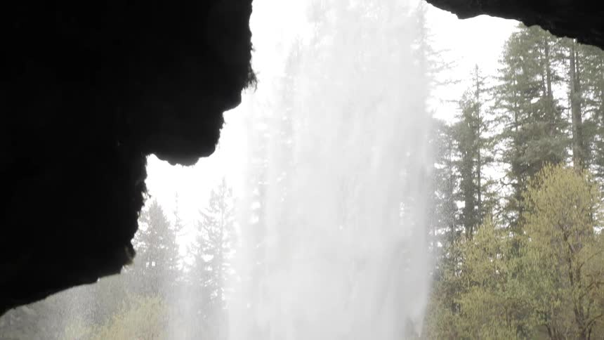 Camera looks out of a cave at a waterfall