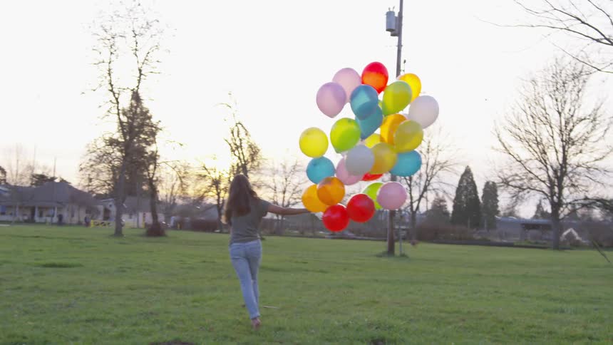 Woman runs across a green field holding balloons