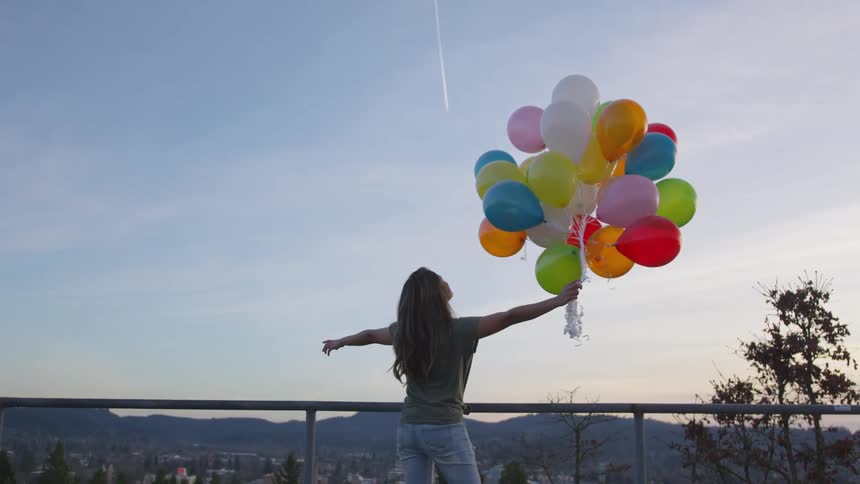 Woman holding several colored balloons while contemplating the horizon
