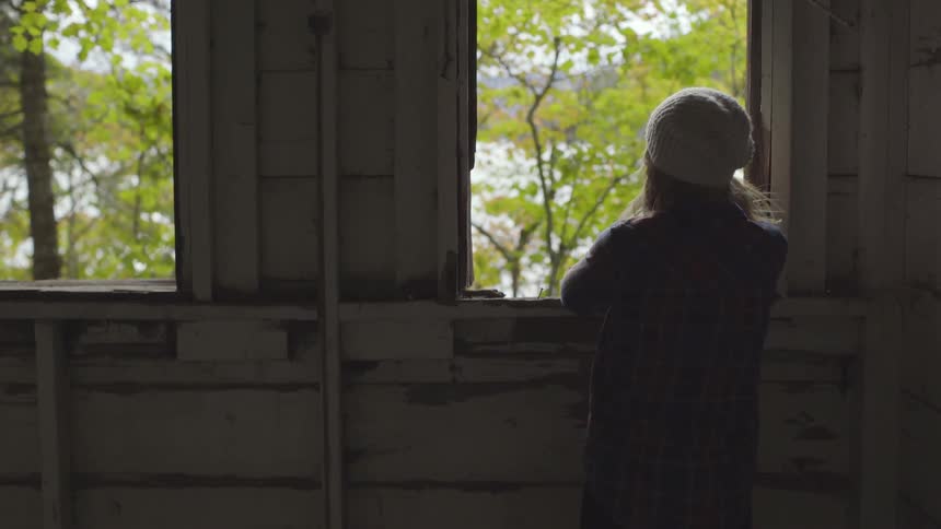 Woman looks out the window of a building into nature
