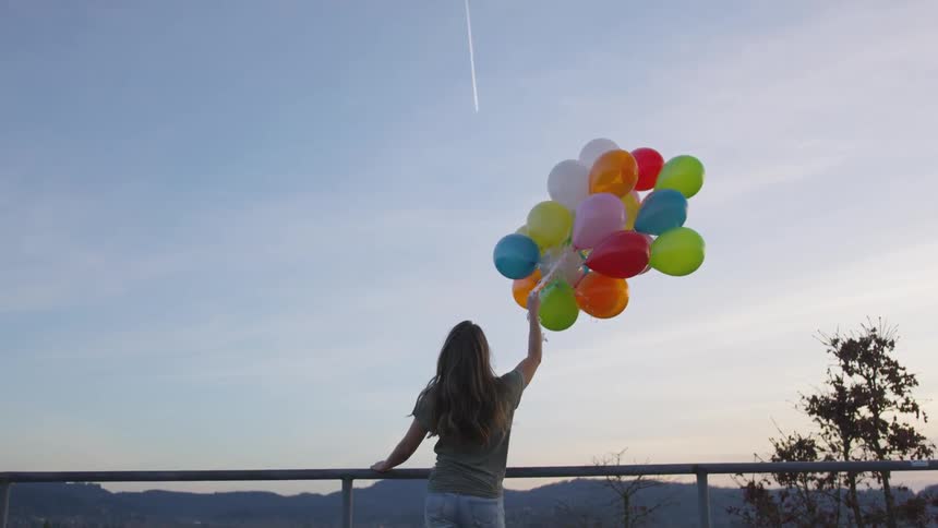 A woman outside standing near railing holding balloons