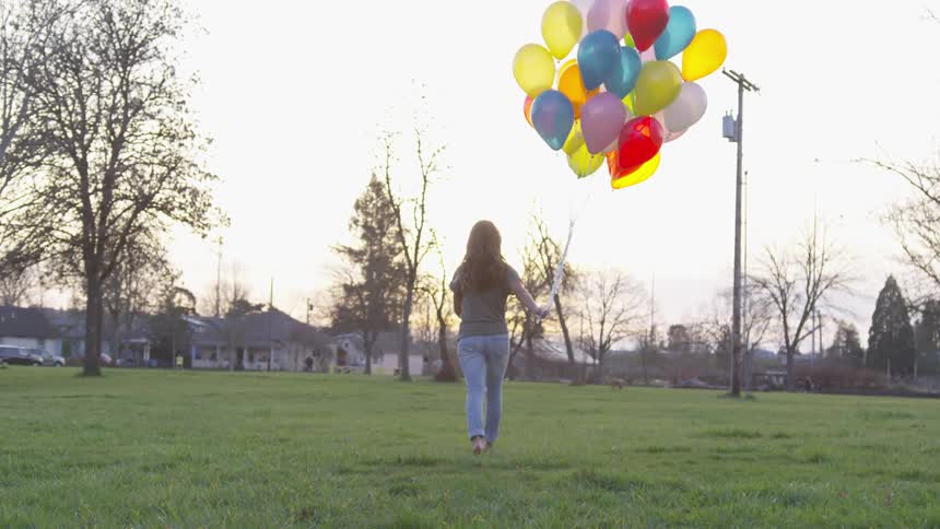 Woman walking in a empty field while holding colored balloons