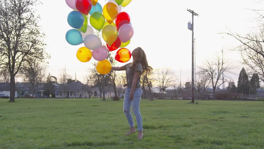 A woman is walking backwards while smiling at a bouquet of balloons