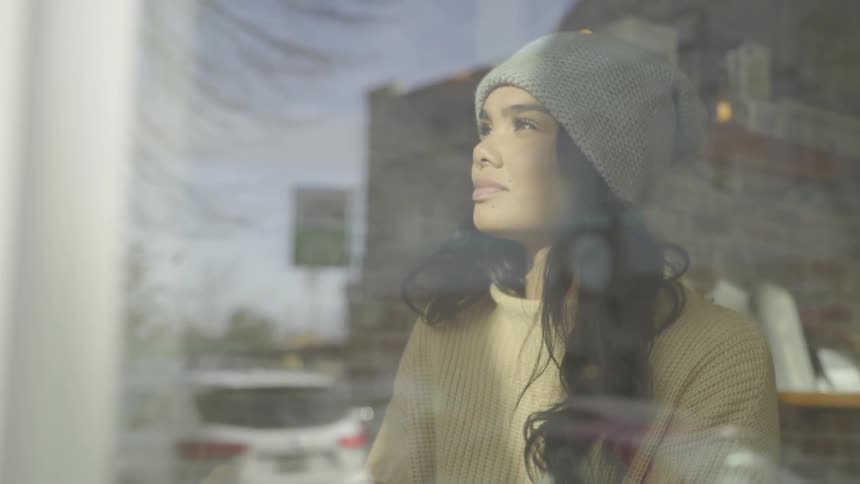 Woman drinking coffee close to a large window