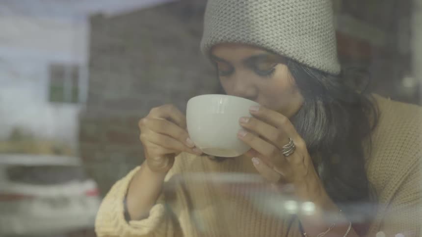 Woman in winter clothes drinking coffee in front of a large window