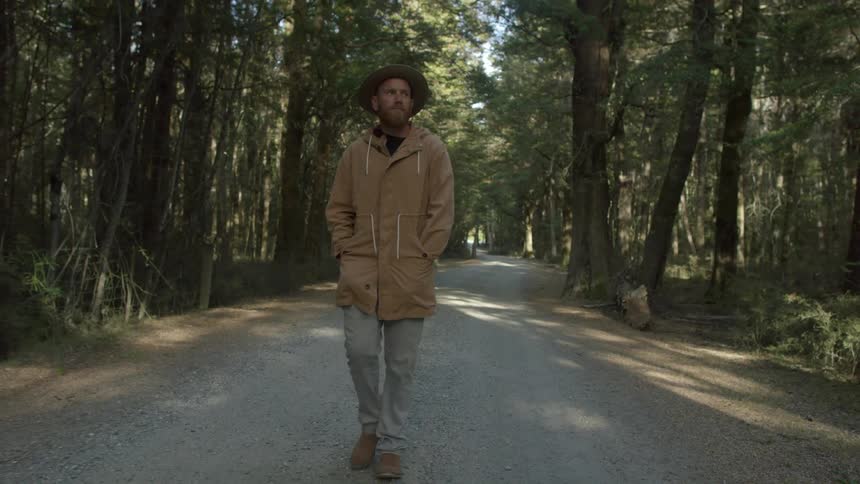Man wearing hat and jacket walks down tree surrounded road