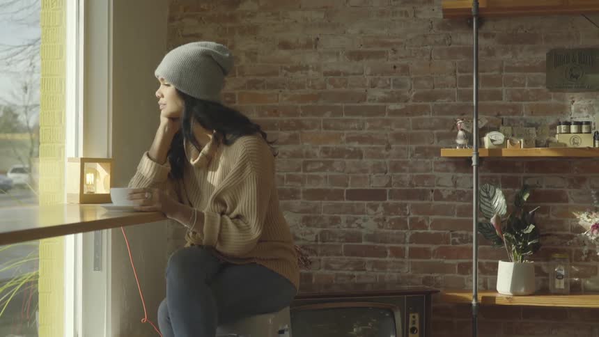 Woman sits inside a cafe with a mug and looks out the window