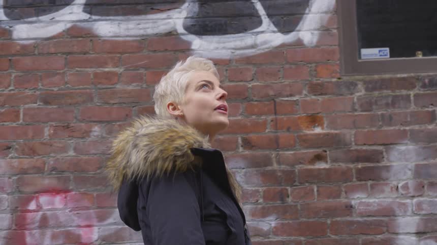 A woman walking down a sidewalk next to a wall with graffiti on it