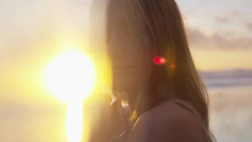 A blonde woman stands outside on a beach at sunset