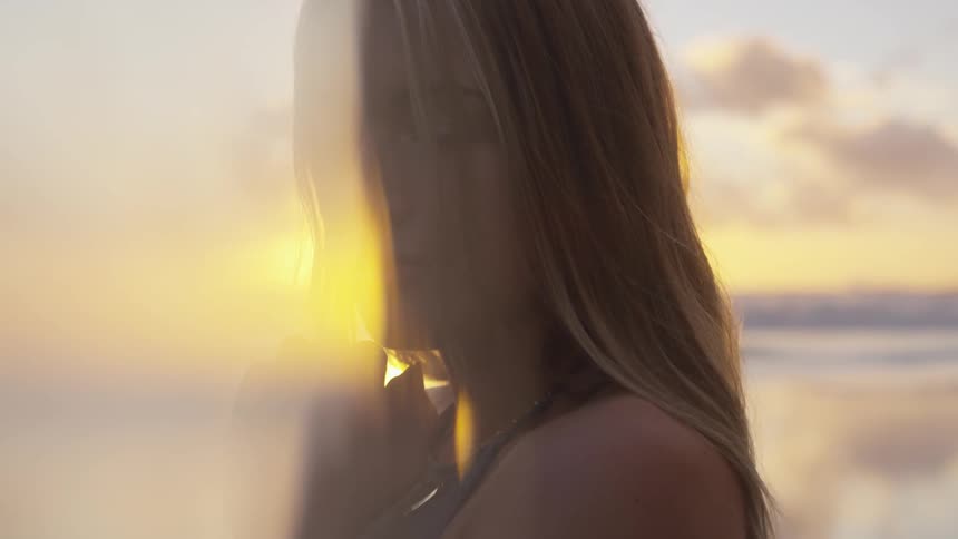 A blonde woman stands on a beach at sunset