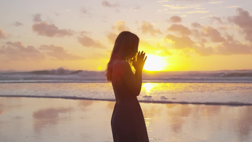 Silhouette of a woman standing on the beach against the sunset