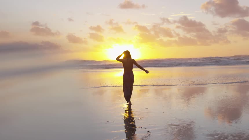 Woman standing on the shore of a beach looking at the sunset over the ocean