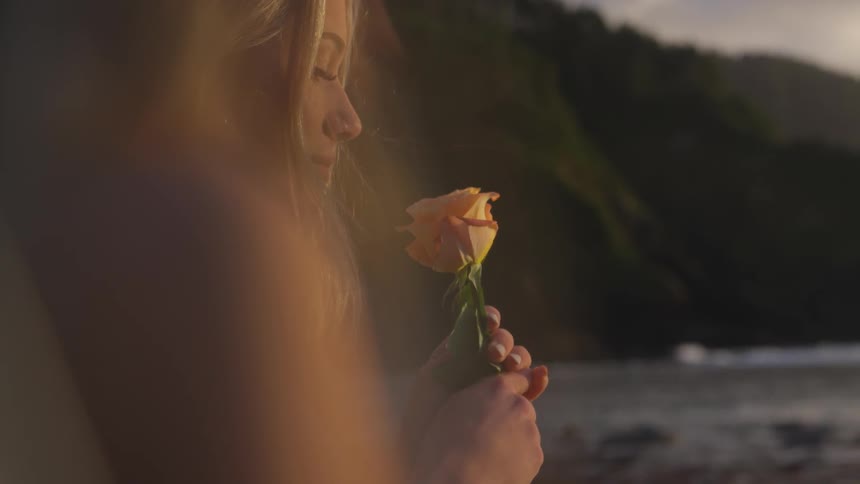 Woman smells a rose next to the ocean
