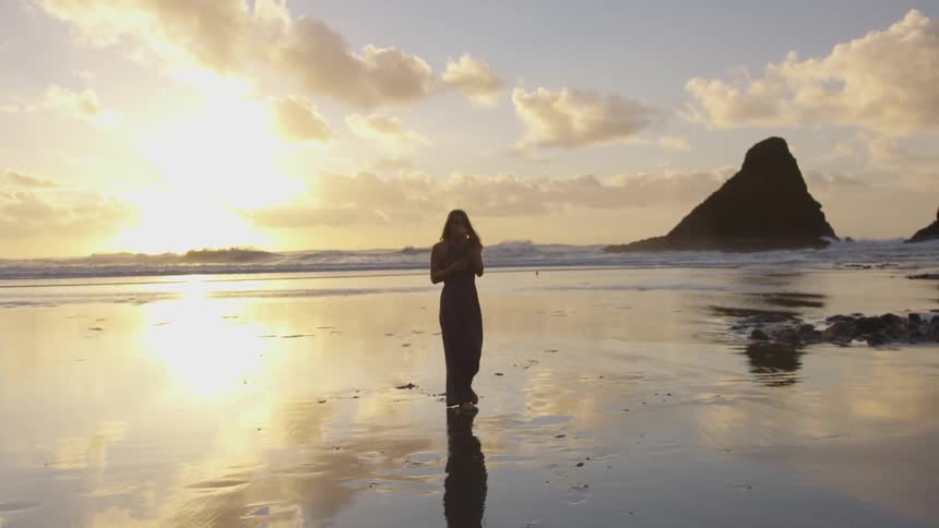 Woman walking down beach with sunset in the background