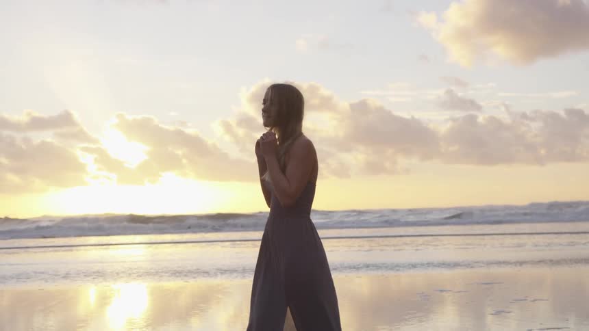 A young woman walks along the beach while playing with her hair