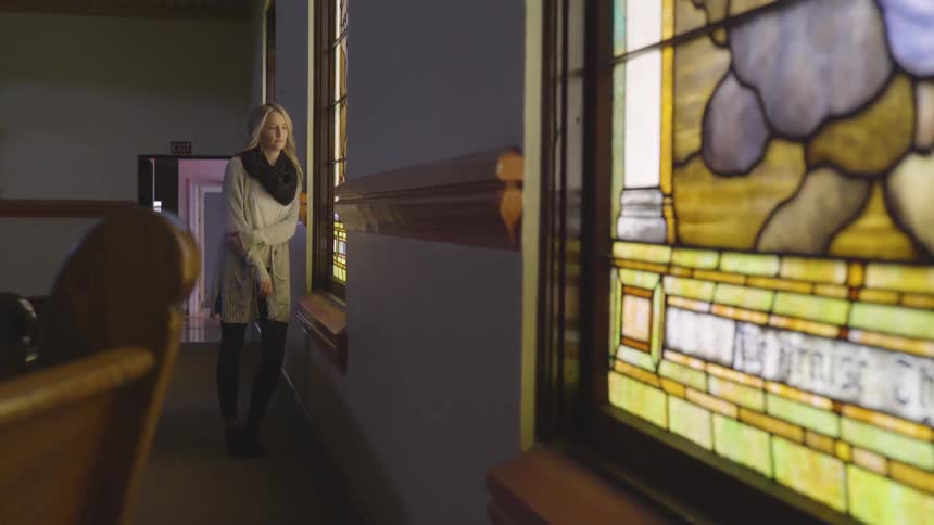 Blonde woman stands and looks out the window indoors
