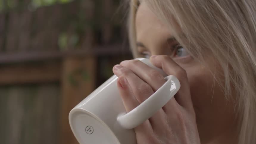 A blonde haired woman is drinking from a mug