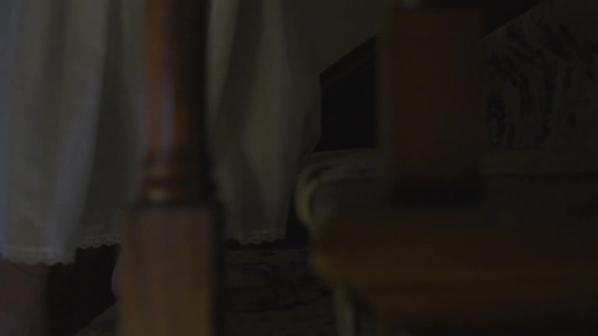 A woman ascends steps in a dark home while wearing a nightgown