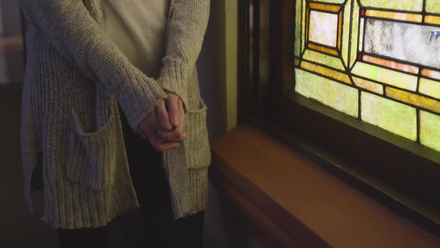 Woman clasping hands stands next to the painted window