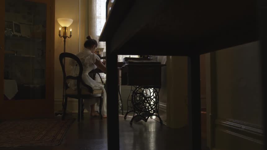 Woman in antique dress sits at vintage sewing machine