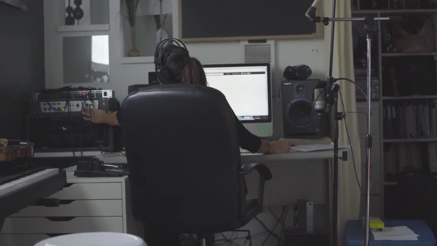 Woman sitting on a chair working on a computer mixing sounds while wearing headphones