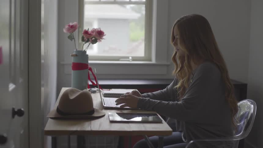 Woman sits at kitchen table working on laptop