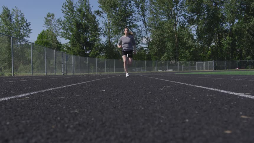 A white female athlete is sprinting down the running track as they prepare themselves for an event