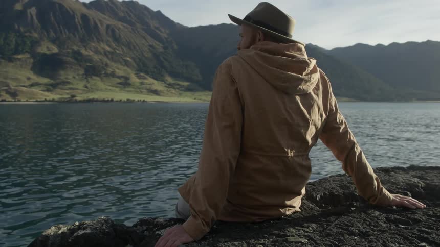 A man sits along a rocky shoreline staring outwards
