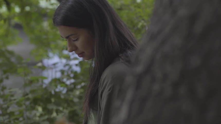 A woman rests her eyes near a tree