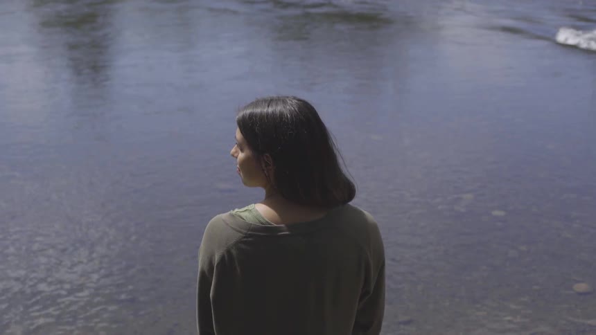 A woman stands and faces a large body of water