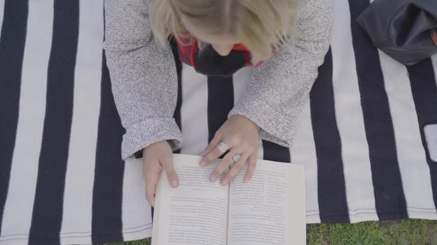 A woman laying on a towel outside reading a book