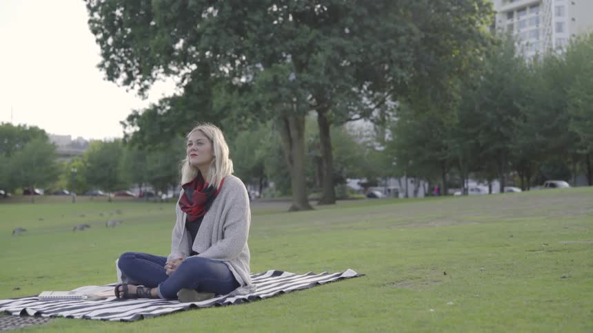 Woman meditates while sitting on towel in park