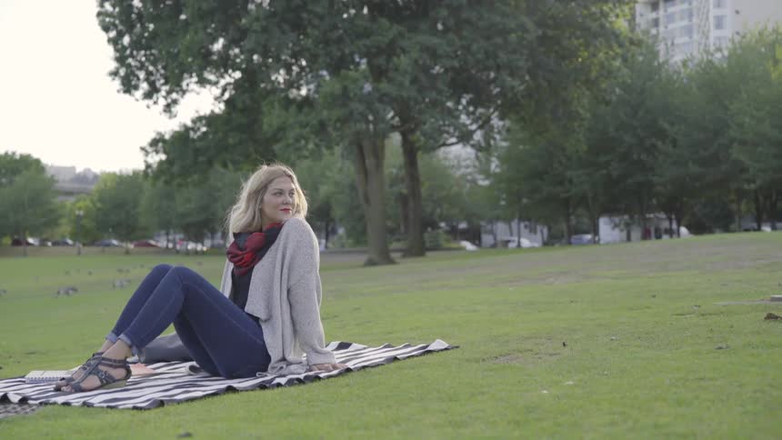 A woman is outdoors sitting on a blanket